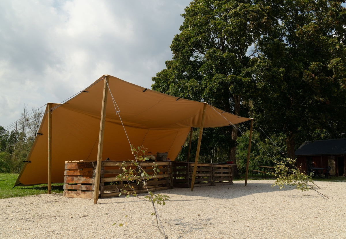 CanvasCamp Heavy Duty Shelter monté avec des mâts en bois au-dessus d'un coin salon sur du gravier