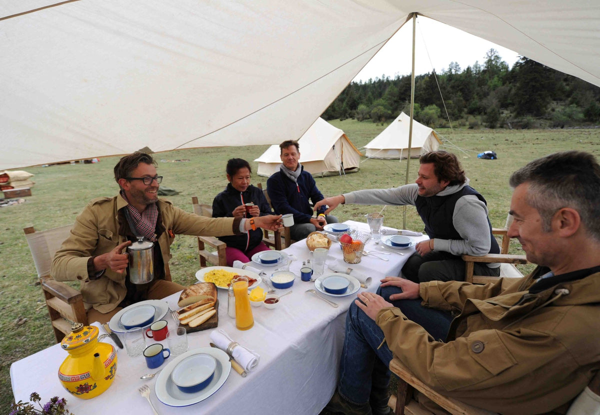Auvent CanvasCamp Malu au-dessus d'une table de petit-déjeuner dressée avec des gens au camping