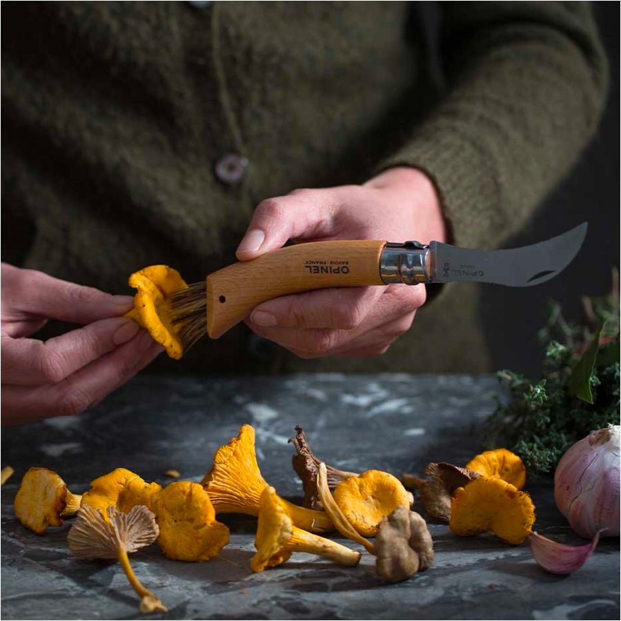 Couteau à champignons Opinel N°08 en usage, des mains brossent des girolles sur un plan en pierre