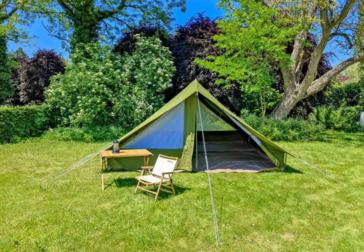 CanvasCamp Patrol Pro avec table pliante et chaise devant la tente ouverte dans un jardin ensoleillé