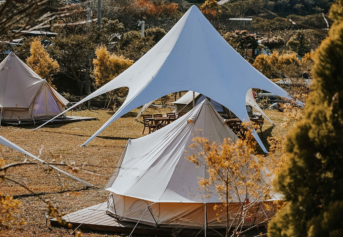 Tente événementielle CanvasCamp StarShade blanche au-dessus d'une tente cloche sur un site de glamping