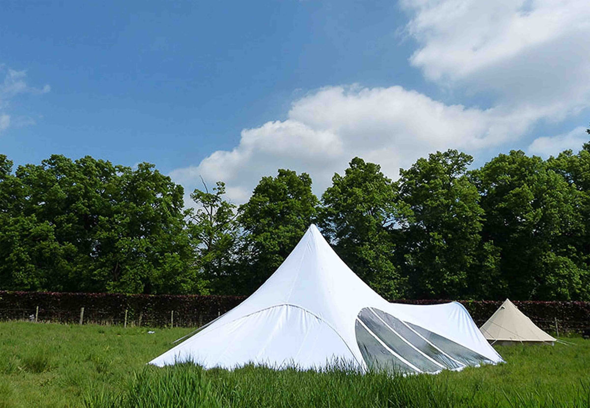 Panneau latéral CanvasCamp Starshade sur une tente blanche, vu de plus loin dans le pré