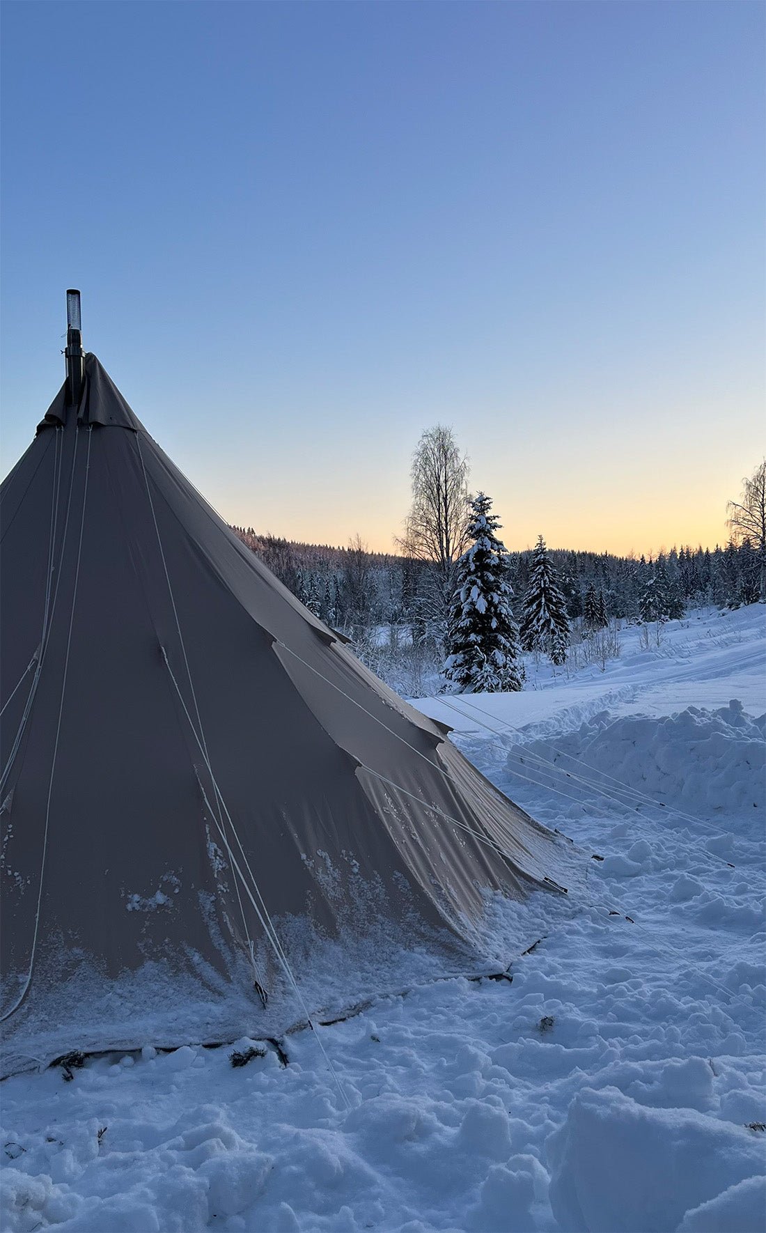 CanvasCamp Traveller 500 dans la neige au coucher du soleil avec tuyau de poêle au sommet