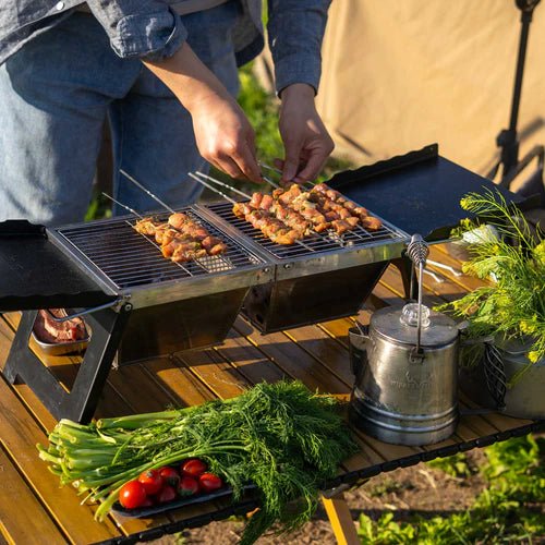Table de camping Winnerwell utilisée comme barbecue au charbon avec brochettes sur le grill dehors