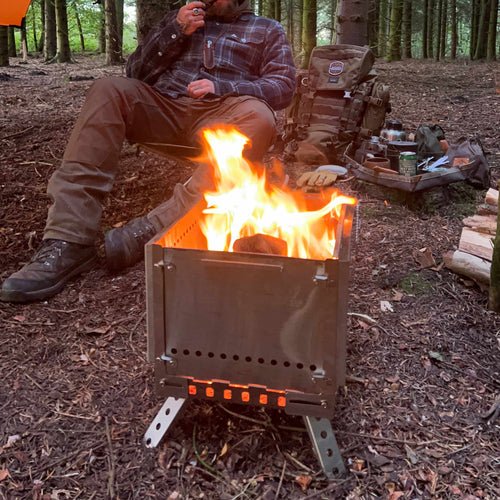 Winnerwell Grill Firepit avec un feu de bois dans la forêt, un homme assis derrière