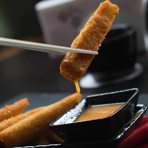Baguettes Winnerwell saisissant un snack frit au-dessus d'un petit bol de sauce